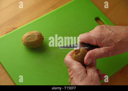 An older man peels a kiwifruit over a green cutting board Stock Photo