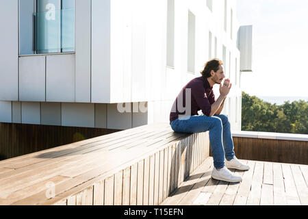 Man sitting on a rooftop terrace, looking worried Stock Photo
