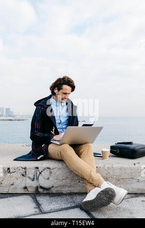 Spain, Barcelona, man sitting at the sea working with laptop and notebook Stock Photo