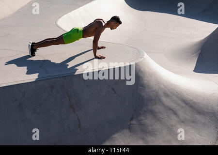 Barechested muscular man doing push-ups in a skatepark Stock Photo