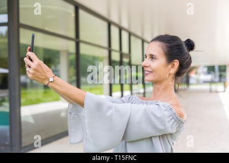Smiling mature woman taking selfie with smartphone outdoors Stock Photo