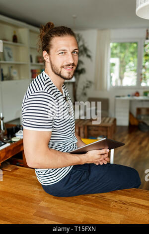 Young man with a bun sitting on table, using digital tablet Stock Photo