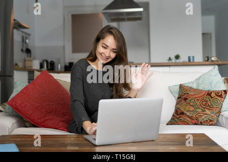 Young woman sitting on her couch, chatting on her laptop Stock Photo