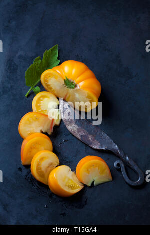 Sliced Azoychka tomato and an old knife on dark ground Stock Photo