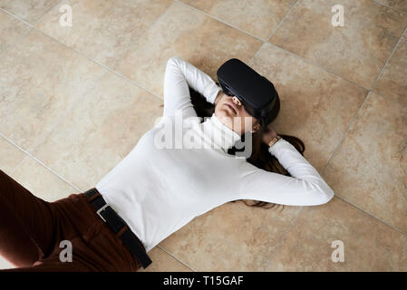 Young woman using virtual reality headsets lying on the floor at home Stock Photo