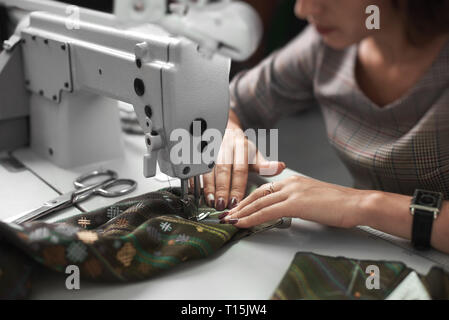 Female seamstress working on modern electrical sewing machine connecting colorful clothing details. Dressmaker making garment in studio. Hobby, do it  Stock Photo