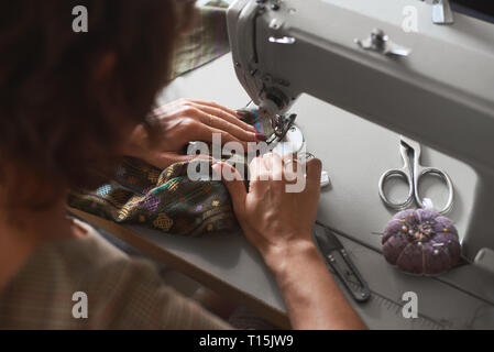 Close-up of female seamstress hands sewing clothing detail on electrical sewing machine. Tailor atelier - handmade exclusive clothes making and repair Stock Photo