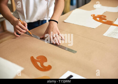 Workplace in design studio. Professional female designer hands close-up making paper patterns using measuring tape, ruler and curves. Exclusive clothe Stock Photo