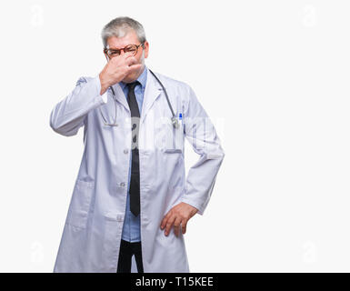 Handsome senior doctor man over isolated background smelling something stinky and disgusting, intolerable smell, holding breath with fingers on nose.  Stock Photo