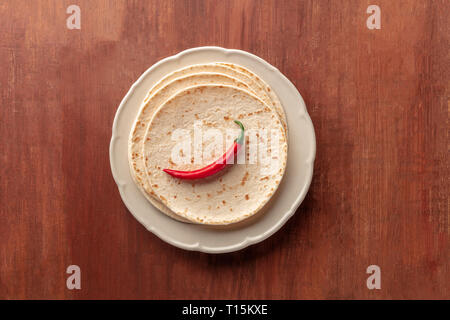 A red chili pepper, shot from above on a pile of tortillas, Mexican flatbreads, on a dark rustic wooden background with copy space Stock Photo