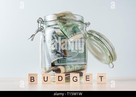 us dollars banknotes in glass jar and word budget made of wooden blocks Stock Photo