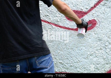 A young hooligan paints graffiti on a concrete wall. Illegal vandalism concept. Street art. Stock Photo