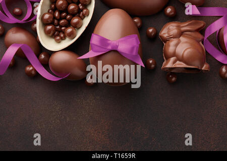 Easter composition with chocolate eggs and bunny decorated with purple ribbon on dark brown background, holiday concept Stock Photo