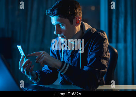 A young man working on a laptop at night. The designer or system administrator stayed late at work. Stock Photo