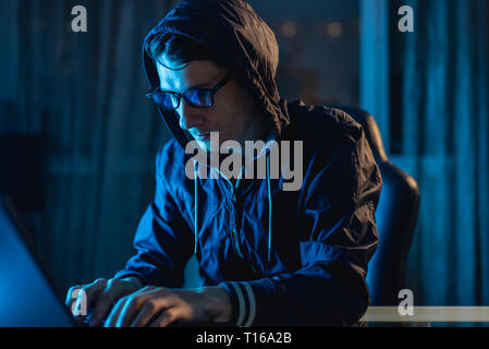 Cybercriminal hacker in the hood typing program code while stealing access databases with passwords. The concept of cyber security Stock Photo