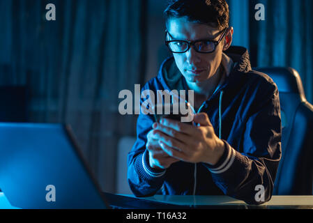 Male hacker in the hood holding the phone in his hands and trying to steal access databases with passwords. The concept of cyber security Stock Photo