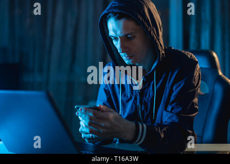 Cybercriminal hacker in the hood typing program code while stealing access databases with passwords. The concept of cyber security Stock Photo