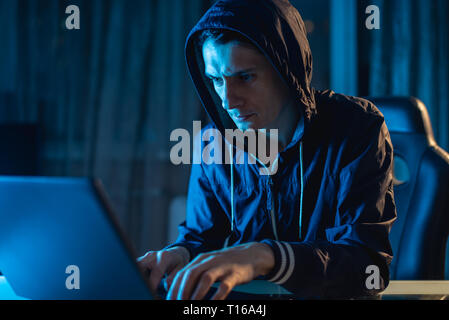 Cybercriminal hacker in the hood typing program code while stealing access databases with passwords. The concept of cyber security Stock Photo