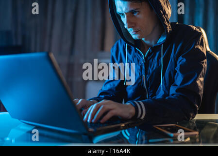 Cybercriminal hacker in the hood typing program code while stealing access databases with passwords. The concept of cyber security Stock Photo