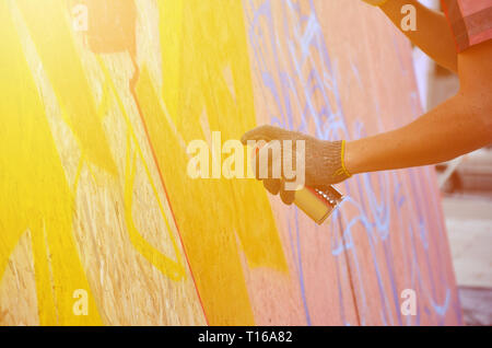 A hand with a spray can that draws a new graffiti on the wall. Photo of the process of drawing a graffiti on a wooden wall close-up. The concept of st Stock Photo