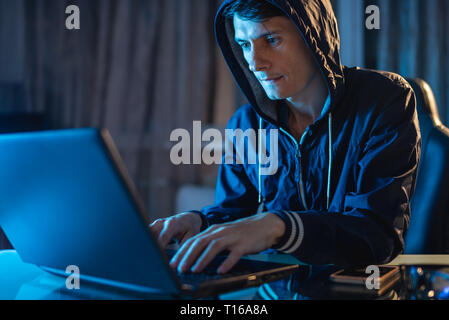 Cybercriminal hacker in the hood typing program code while stealing access databases with passwords. The concept of cyber security Stock Photo