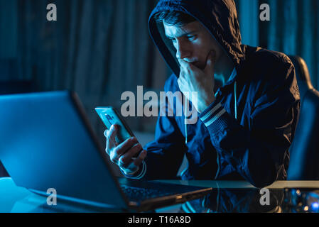 Hacker in the hood holding the phone in his hands trying to steal access databases with passwords. The concept of cyber security