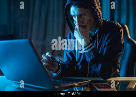 A male hacker in glasses thinking about the problem of hacking and stealing access databases with passwords. The concept of cybersecurity Stock Photo