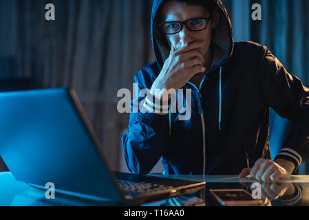 A male hacker in glasses thinking about the problem of hacking and stealing access databases with passwords. The concept of cybersecurity Stock Photo