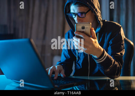 Hacker in the hood holding the phone in his hands trying to steal access databases with passwords. The concept of cyber security Stock Photo