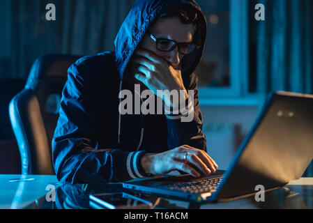 A male hacker in glasses thinking about the problem of hacking and stealing access databases with passwords. The concept of cybersecurity Stock Photo