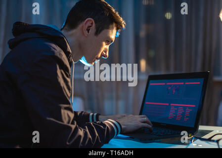 A young man working on a laptop at night. The designer or system administrator stayed late at work. Stock Photo