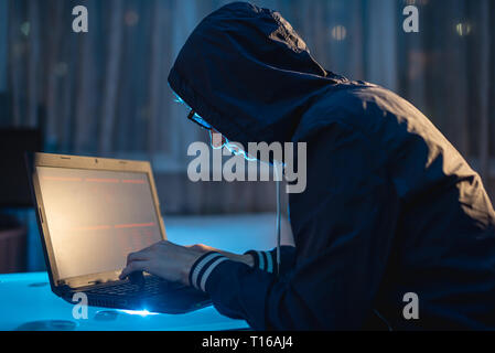 Cybercriminal hacker in the hood typing program code while stealing access databases with passwords. Hackers and cyber security concept Stock Photo