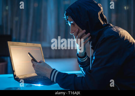 Cybercriminal hacker in the hood typing program code while stealing access databases with passwords. Hackers and cyber security concept Stock Photo