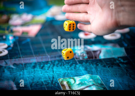 Hand throws two yellow dice on the blue playing field. Gaming moments in dynamics. Luck and excitement. Board games strategy Stock Photo