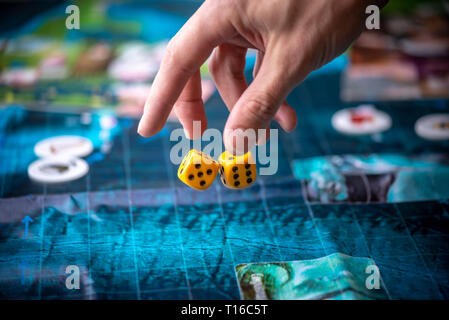 The hand throws two yellow dice on the playing field. Gaming moments in dynamics. Luck and excitement. Board games strategy Stock Photo