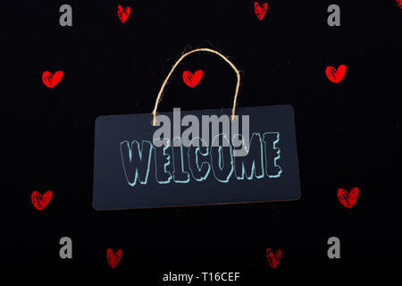 Welcome wording on black notice board  with red hearts around Stock Photo