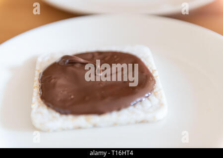 Closeup of rice cake with chocolate hazelnut spread with brown syrup vegan vegetarian snack dessert one single piece on white plate Stock Photo