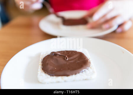 Closeup of rice cake with chocolate hazelnut spread woman spreading with spoon brown syrup vegan vegetarian snack dessert one single piece on white pl Stock Photo