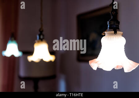Closeup of three hanging ceiling lamps in home with dark room and illuminated yellow green fixtures in row Stock Photo