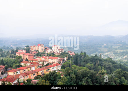Chiusi village cityscape in Tuscany Italy with orange red rooftop tile houses on mountain countryside and rolling hills with morning mist haze fog Stock Photo