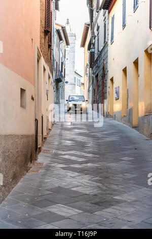 Chiusi, Italy - August 25, 2018: Street in small town village in Umbria Tuscany narrow vertical view during day with orange pink yellow walls and car  Stock Photo