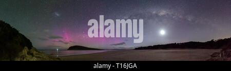 Panorama of the Milky Way with the moon underneath and a disaplay of the Aurora Australis or Southern Lights over a beach in Tasmania. Stock Photo