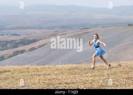 Woman running freedom in Val D'Orcia autumn countryside in Tuscany, Italy with farm landscape picturesque meadow and girl in dress travel Stock Photo