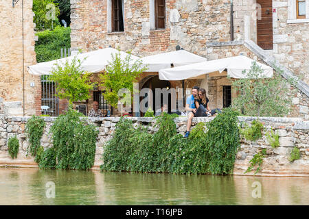 Bagno Vignoni, Italy - August 26, 2018: Medieval town by San Quirico d'Orcia in Val d'Orcia, Tuscany with people tourists romantic couples sitting by  Stock Photo