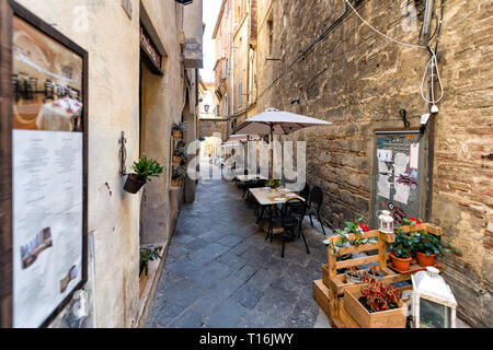 Siena, Italy - August 27, 2018: Alley narrow street in historic medieval old town village in Tuscany with nobody and restaurant tables outside outdoor Stock Photo