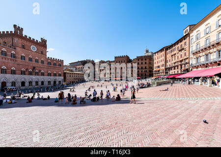 Siena, Italy - August 27, 2018: Street piazza in historic medieval old town village in Tuscany with crowd of many people tourists travel walking sitti Stock Photo