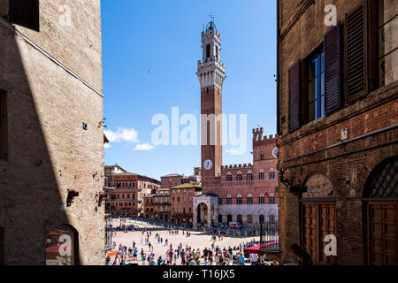 Siena, Italy - August 27, 2018: Street alley framing piazza square in historic medieval old town village in Tuscany with crowd of many people tourists Stock Photo