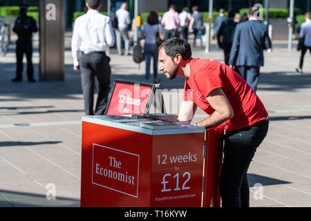 London, UK - June 26, 2018: People crowd commuters outside during morning commute in Canary Wharf with Economist magazine booth closeup Stock Photo