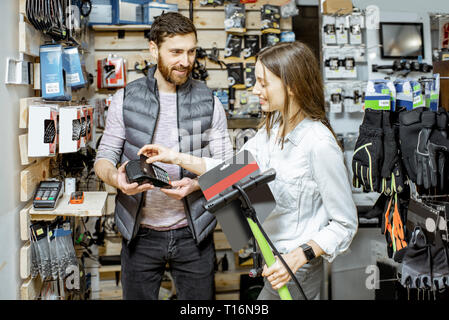 Salesman with young woman buying bicycle pump, paying with card at the sports shop Stock Photo