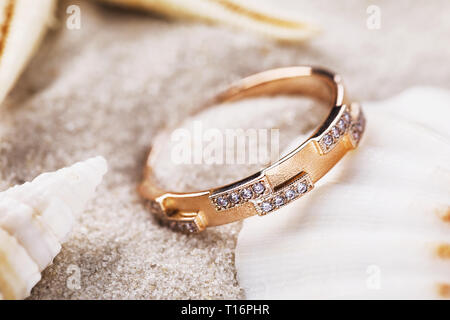 Golden ring decorated with small precious stones on the sand with seashells, close-up Stock Photo